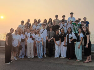 Students having their photograph taken in front of the sea behind a sunset.