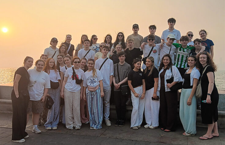 Students having their photograph taken in front of the sea behind a sunset.